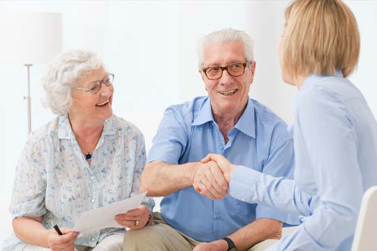 An audiologist making a home visit to an elderly couple with hearing loss.